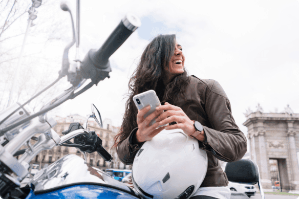 A person sitting on their motorcycle with their helmet and phone in their hands.