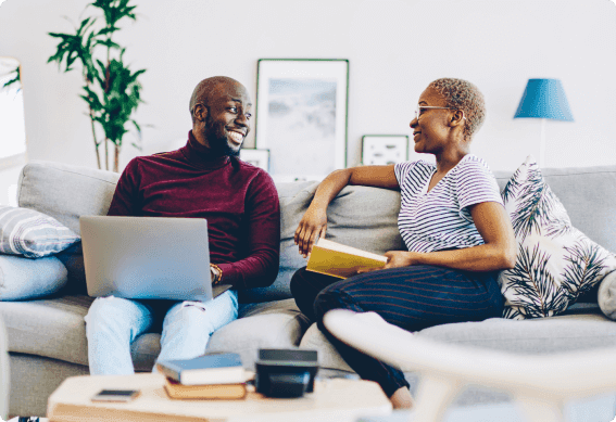 a man and a woman sitting on a couch looking at a laptop