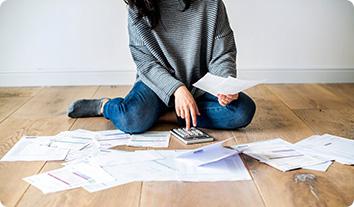 A person sitting on the floor with a calculator and papers