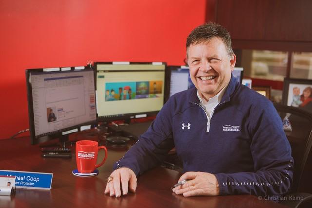 a man sitting at a desk with a computer and a cup