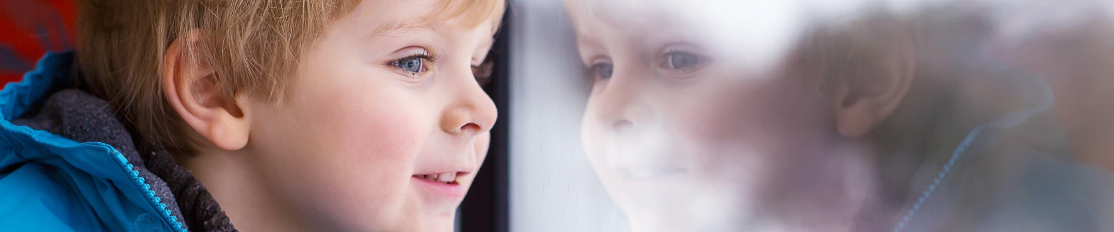 Little boy looking outside a window, dressed in a winter coat