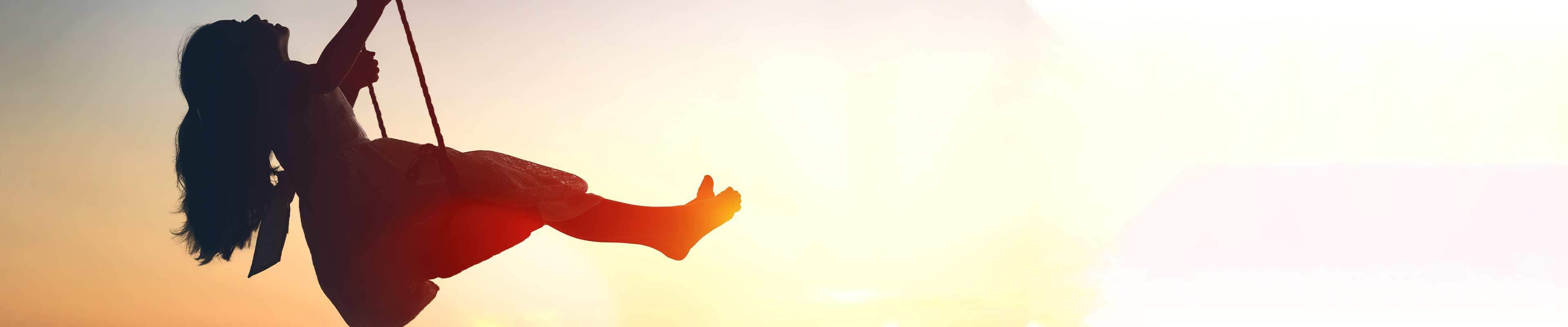 A child swings on a swing before a sun at dusk