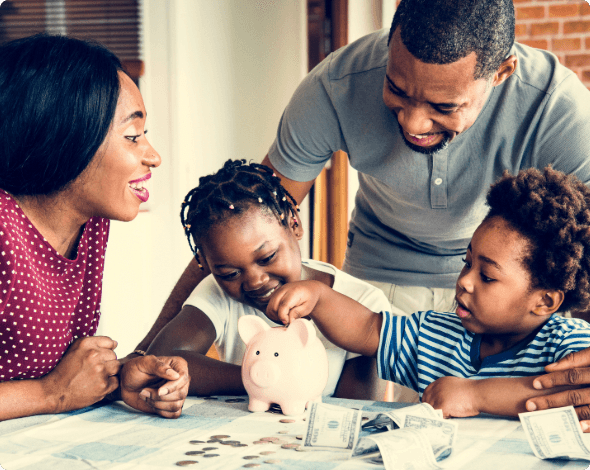 A happy family sitting together at a table, placing money in a piggy bank.