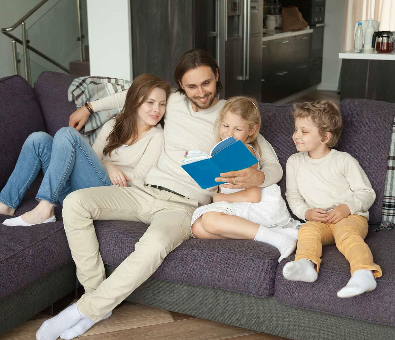 Image of a family on a living room couch reading a book together.