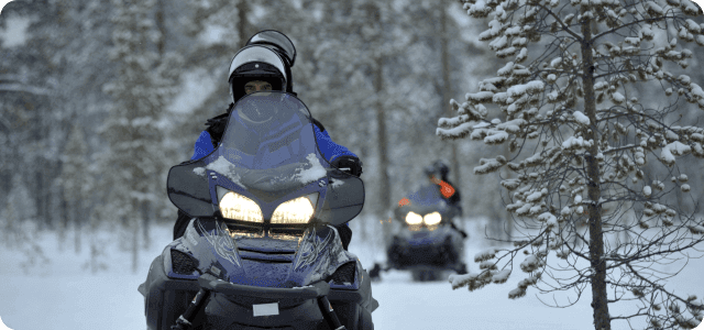 A couple of people riding snowmobiles at dusk