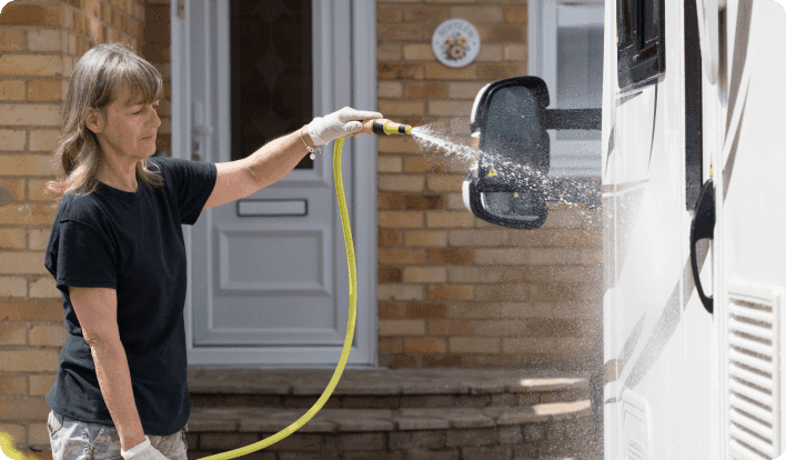 A woman washing washing an RV with a water hose